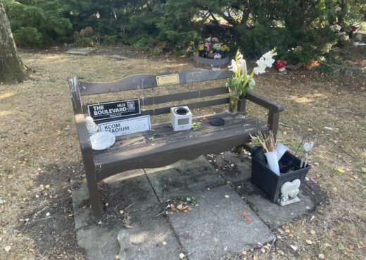 Weathered memorial bench with Hull FC tributes, flowers and keepsakes in the grounds at Chanterlands Crematorium.