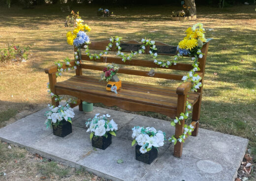 Well-maintained Woodcraft memorial bench decorated with flowers and garlands in the grounds of Chanterlands Crematorium in Hull.