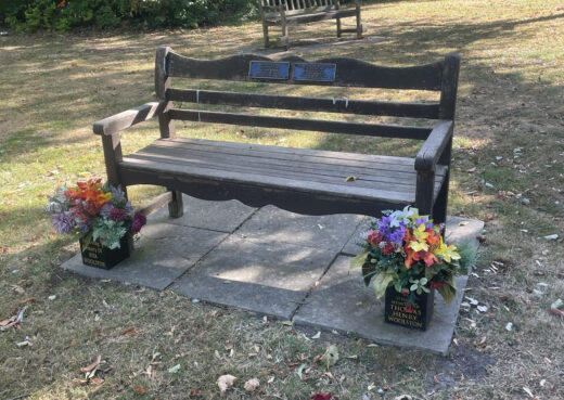Long-standing Woodcraft Beverley memorial bench with dedication plaques and fresh floral tributes in the crematorium grounds.