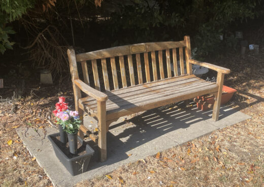 Naturally weathered wooden memorial bench with carved In Loving Memory inscription and flowers at Chanterlands Crematorium.