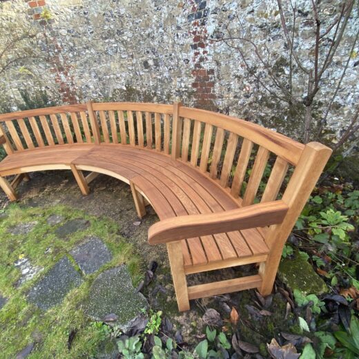 Angled view of a bespoke curved wooden bench designed to follow the line of a historic garden wall at the Hospital of St Cross, Winchester