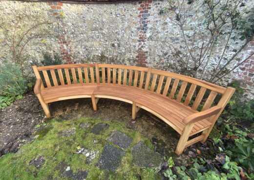 Wide view of the bespoke curved bench set into The Master’s Garden, framed by historic flint walls and planting