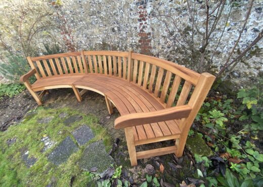 Angled view of a bespoke curved wooden bench designed to follow the line of a historic garden wall at the Hospital of St Cross, Winchester