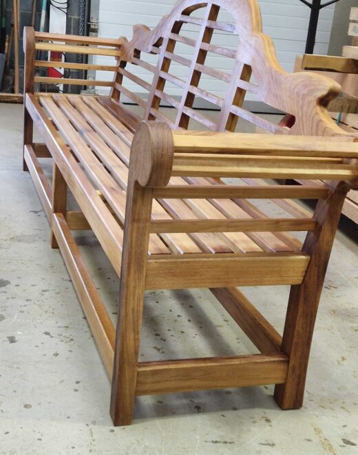 Three-quarter rear view of a bespoke Lutyens-style bench in teak oil showcasing elegant scroll arms and traditional craftsmanship.