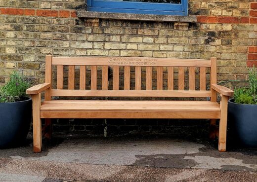 Front view of the handcrafted iroko York memorial bench engraved for Johnny Morrison with decorative planters.