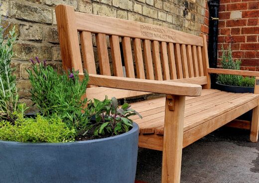 Side view of the Johnny Morrison memorial bench showing the iroko craftsmanship, planter display and QR code linking to Johnny's story.