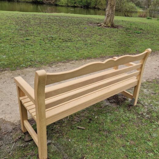 Rear view of wooden park bench near trees and open grass area