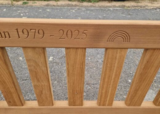 Close-up of memorial bench engraving with rainbow motif and dates 1979–2025