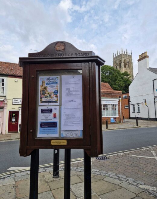 Wooden community notice board with St Augustine's Church visible in the background in Hedon, East Yorkshire.