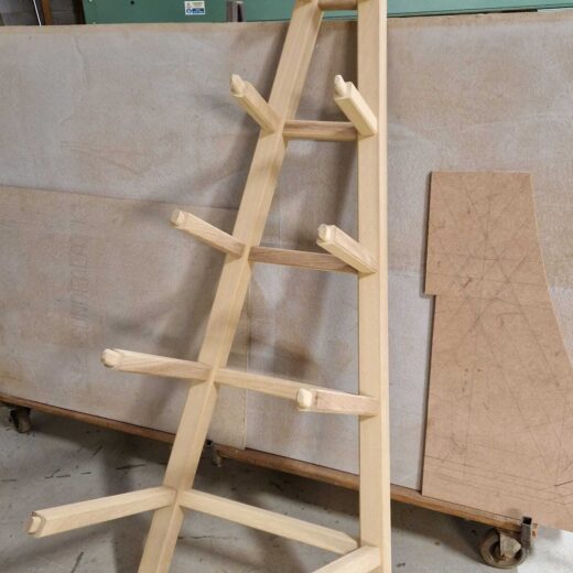 Side panel of a wooden obelisk with support arms attached, photographed upright in the workshop.