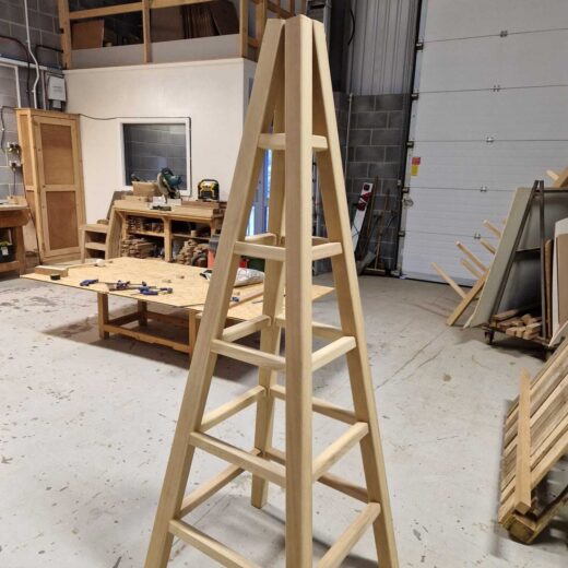 Partially assembled obelisk frame leaning upright, showing the structure and support arms without the top finial