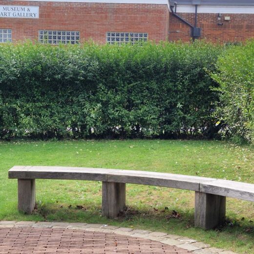 Weathered curved wooden bench at Pannett Park with Whitby Museum and Pannett Art Gallery in the background