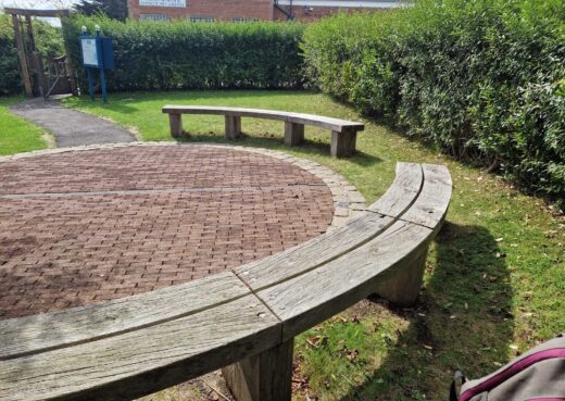 Weathered curved wooden bench at Pannett Park with Whitby Museum and Pannett Art Gallery in the background