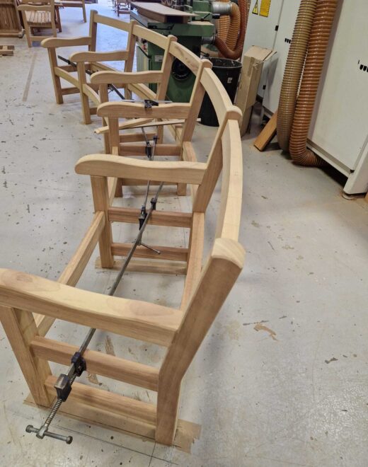 Curved York bench frames in mid-assembly side view at the Woodcraft UK workshop, showing the precision alignment and shaping required to create continuous curved seating for Greenwich Park