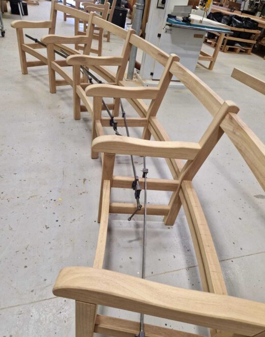 Curved hardwood bench frames lined up in the Woodcraft UK workshop during construction, highlighting the flowing back rails and handcrafted arm details before final assembly