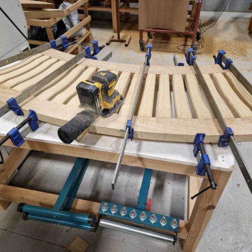 Seat section of the curved Scarborough bench under construction with clamps and sander.